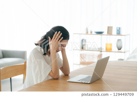 A young woman holding her head in front of a personal computer 129449709