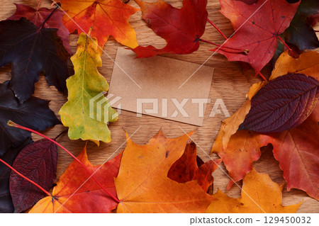 Autumn theme background with leaves over oak wood table with brown paper card 129450032
