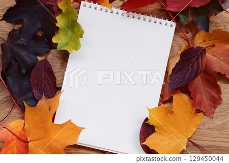 Autumn theme background with leaves over oak wood table with notepad 129450044