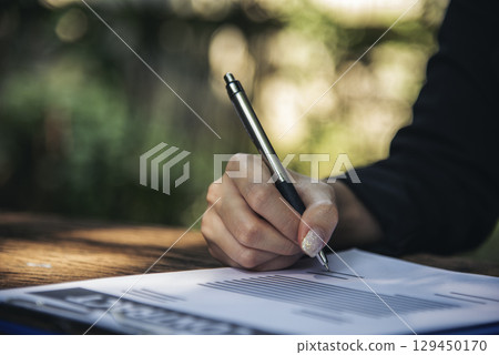 Woman hands writing empty notebook planing meeting agenda on wooden table. Close up women hands using pen drinking coffee cup planning office paper. Female hand holding pen note Personal Organizer 129450170