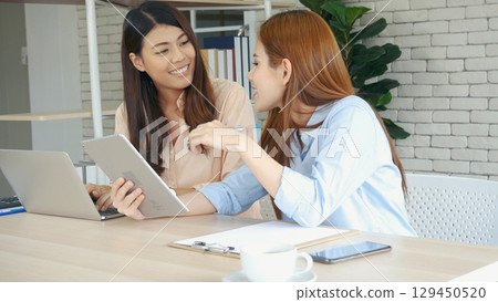Two asian Female freelance reading financial graph charts Planning analyzing marketing data. Asian people team working office firm. Two businesswomen team meeting using laptop at company office desk. 129450520