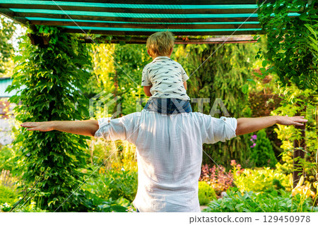 Arms wide as Dad carries toddler under green arbor Arms wide as Dad carries toddler under green arbor 129450978