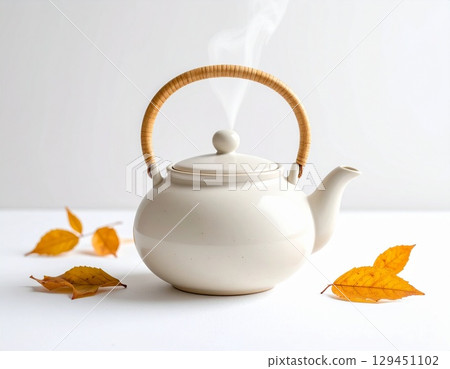白色背景上，一個簡單的陶瓷茶壺冒著熱氣。這是一張極簡主義的秋季熱飲圖片。 129451102