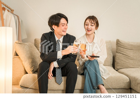 Young Asian couple drinking beer while sitting on the sofa after returning home at night 129451151