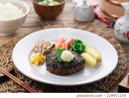 A steaming Japanese-style hamburger steak with grated daikon radish and colorful vegetables. Perfect for a warm home-cooked meal or restaurant menu. A steaming Japanese-style hamburger steak with grated daikon radish and colorful vegetables. Perfect for a warm home-cooked meal or restaurant menu. 129451159