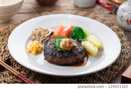 A steaming Japanese-style hamburger steak with grated daikon radish and colorful vegetables. Perfect for a warm home-cooked meal or restaurant menu. 129451163
