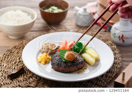 A steaming Japanese-style hamburger steak with grated daikon radish and colorful vegetables. Perfect for a warm home-cooked meal or restaurant menu. A steaming Japanese-style hamburger steak with grated daikon radish and colorful vegetables. Perfect for a warm home-cooked meal or restaurant menu. 129451164