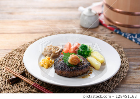 A steaming Japanese-style hamburger steak with grated daikon radish and colorful vegetables. Perfect for a warm home-cooked meal or restaurant menu. A steaming Japanese-style hamburger steak with grated daikon radish and colorful vegetables. Perfect for a warm home-cooked meal or restaurant menu. 129451168
