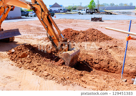 Heavy machinery works to dig trench into ground at construction site Heavy machinery works to dig trench into ground at construction site 129451383