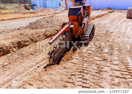 Construction crew utilizes trenching machine to create deep trench for utility lines at building site 129451387