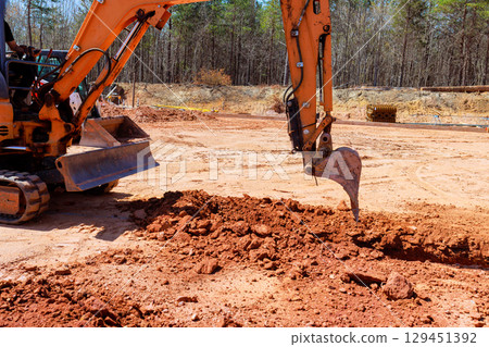 Excavator actively digs large trench of dirt at rural construction site. 129451392
