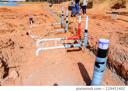 Workers are installing plumbing pipes in newly excavated area at construction site 129451402