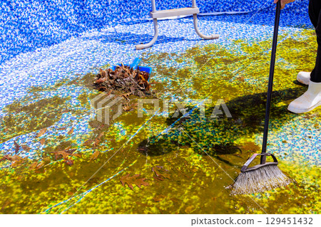Worker cleans algae debris from bottom of swimming pool in private garden under works day 129451432