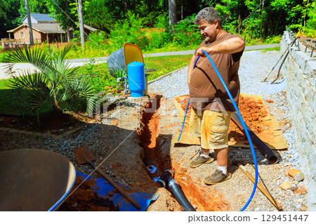 Individual is installing an water pump well system in yard while managing tools materials 129451447