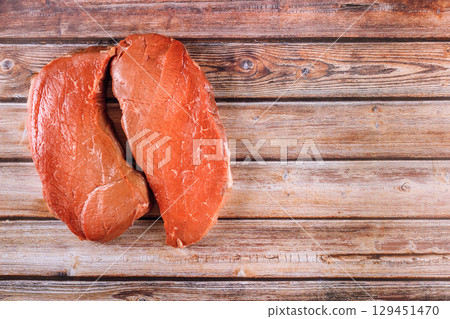 Two raw beef steaks are placed side by side on an aged wooden table in kitchen environment. 129451470