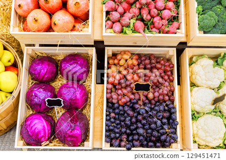 Colorful assortment of fruits vegetables neatly arranged in wooden crates at an outdoor market. Colorful assortment of fruits vegetables neatly arranged in wooden crates at an outdoor market. 129451471