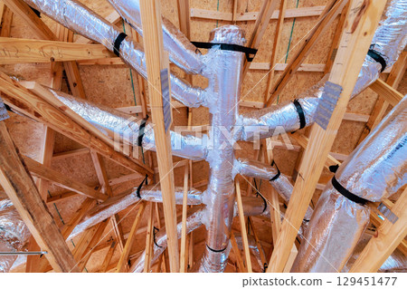 Ducts are placed among wooden beams in house being built, highlighting ventilation system setup. 129451477