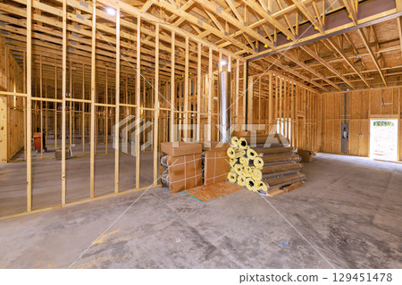 Interior view of building under construction with wooden frames, insulation rolls, open residential area space. Interior view of building under construction with wooden frames, insulation rolls, open residential area space. 129451478