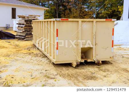 Large waste container sits on construction site surrounded by wooden pallets debris during works day hours. Large waste container sits on construction site surrounded by wooden pallets debris during works day hours. 129451479