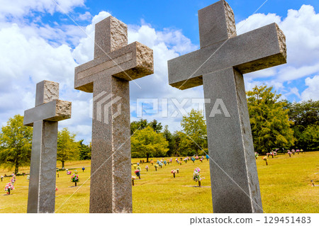 Three tall crosses stand in peaceful cemetery surrounded by greenery flower arrangements. Three tall crosses stand in peaceful cemetery surrounded by greenery flower arrangements. 129451483