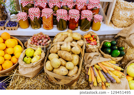 Vibrant display of fresh fruits, vegetables, jars of homemade preserves at farmers market in lively setting. 129451495