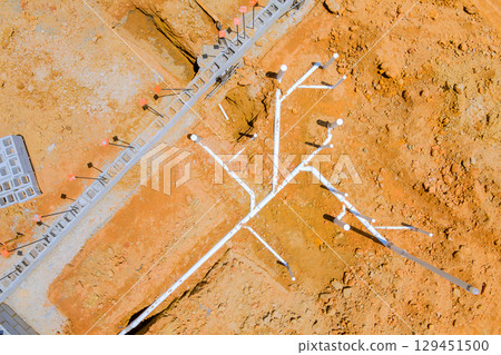 Detailed view of construction site displaying intricate PVC piping plumbing installation configurations on dry terrain. 129451500
