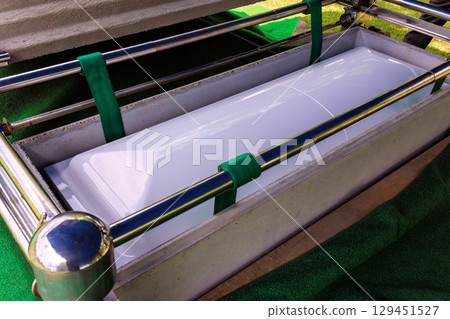 White casket in metal frame is surrounded by green fabric at an outdoor memorial in tranquil cemetery 129451527