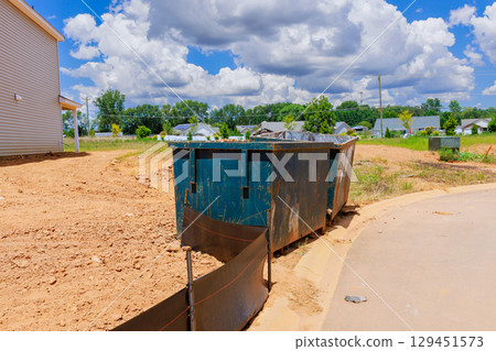 Temporary dumpster sits in construction zone surrounded by bare soil new houses under works day 129451573