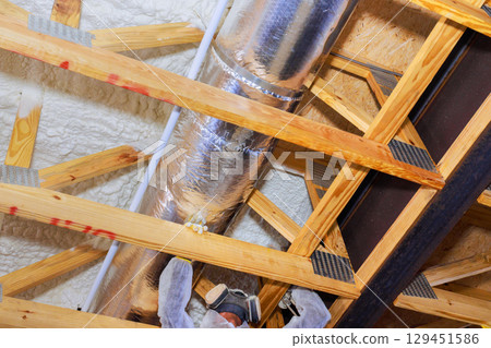 Worker are fitting thermal barrier insulation around metallic duct in new home ceiling. 129451586