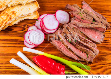 Grilled steak is beautifully arranged with sliced radishes, green onions, flatbread, an appetizing creating 129451606