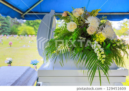 Beautiful arrangement of flowers adorns casket at an outdoor burial ceremony in tranquil cemetery. 129451609