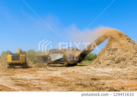 Large machine piles wood chips while another aids in land clearing dusty background. 129451610