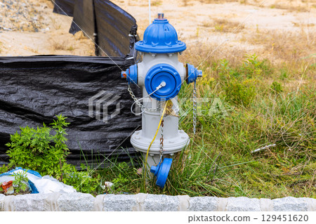 Blue, gray hydrant stands in construction zone, surrounded by grass debris, ready for emergencies. 129451620