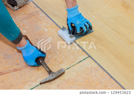 Hands fitting laminate flooring together using tapping block hammer for proper alignment secure placement. 129451623