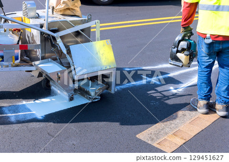 Workers are using road marking machine to apply white paint on new asphalt surface in city setting. 129451627