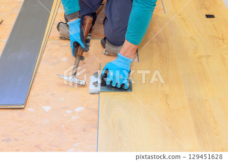 Craftsman carefully places secures wooden planks on floor, demonstrating precise techniques. 129451628