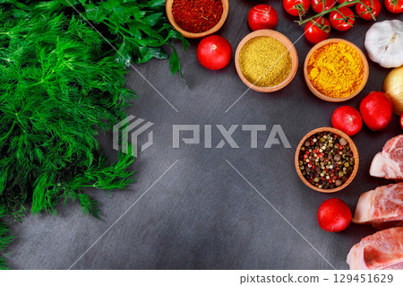 Fresh herbs, spices, vegetables, raw meats arranged artfully on dark countertop ready for cooking meal preparation Fresh herbs, spices, vegetables, raw meats arranged artfully on dark countertop ready for cooking meal preparation 129451629