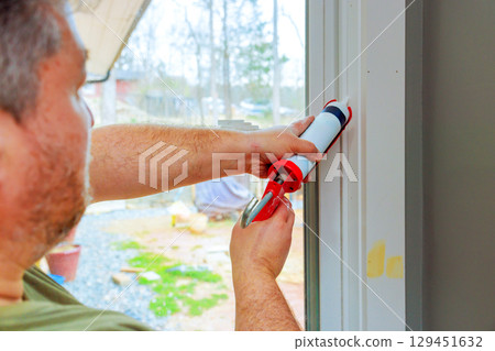 Homeowner prepares to apply caulk around window frame for insulation protection against weather elements. Homeowner prepares to apply caulk around window frame for insulation protection against weather elements. 129451632