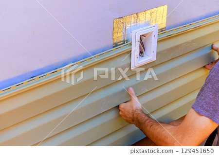 Worker carefully fits vinyl siding panels onto building exterior, ensuring precise alignment fit for durability. 129451650