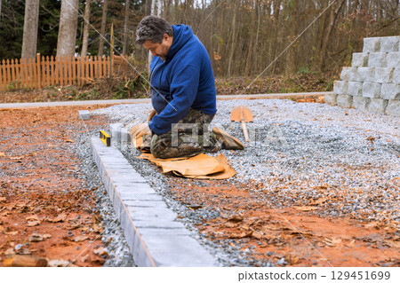 Craftsman prepares ground arranges stones for new patio in residential area surrounded by trees Craftsman prepares ground arranges stones for new patio in residential area surrounded by trees 129451699