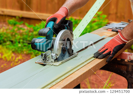 Worker uses circular saw to cut vinyl facade siding at home improvement efforts. 129451700