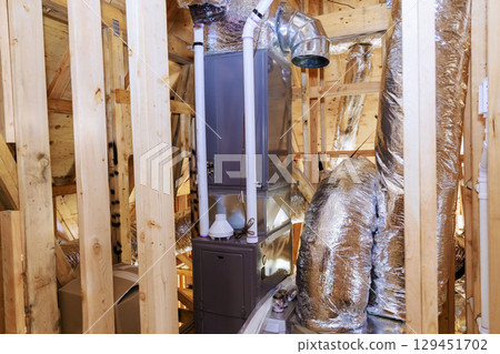 Workers install heating unit in an attic with wooden framing ductwork in residential building. 129451702