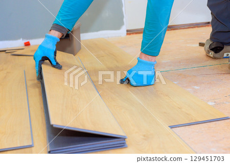 Contractor is laying laminate flooring in home while wearing protective gloves on task. Contractor is laying laminate flooring in home while wearing protective gloves on task. 129451703