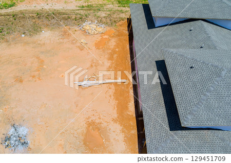 New home construction features new shingles finished at roof an unfinished site with debris scattered nearby. 129451709