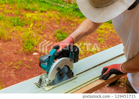 Carpenter is operating circular power saw on vinyl siding plank while working on construction project outside. Carpenter is operating circular power saw on vinyl siding plank while working on construction project outside. 129451715