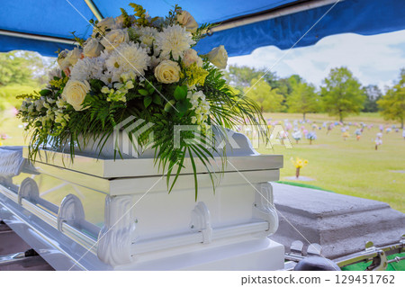 Floral arrangement atop an elegant casket at peaceful burial site surrounded by gravestones 129451762