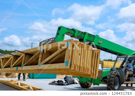 Construction activity unfolds as workers operate machinery to lift large wooden beams truss at building site. 129451783