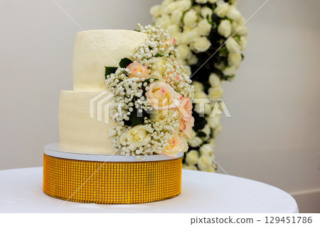Two tiered cake decorated with fresh roses delicate flowers at wedding reception during springtime. 129451786
