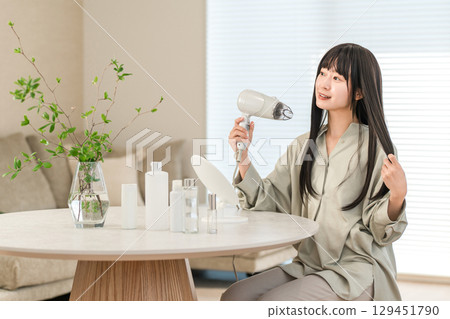 A woman blow-drying her hair with a hair dryer (hair care) 129451790