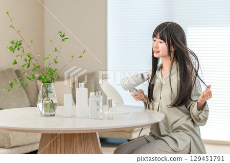 A woman blow-drying her hair with a hair dryer (hair care) 129451791